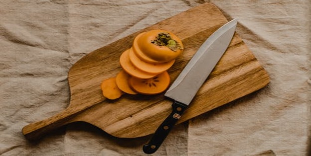 A knife and a sliced persimmon on a wooden chopping board